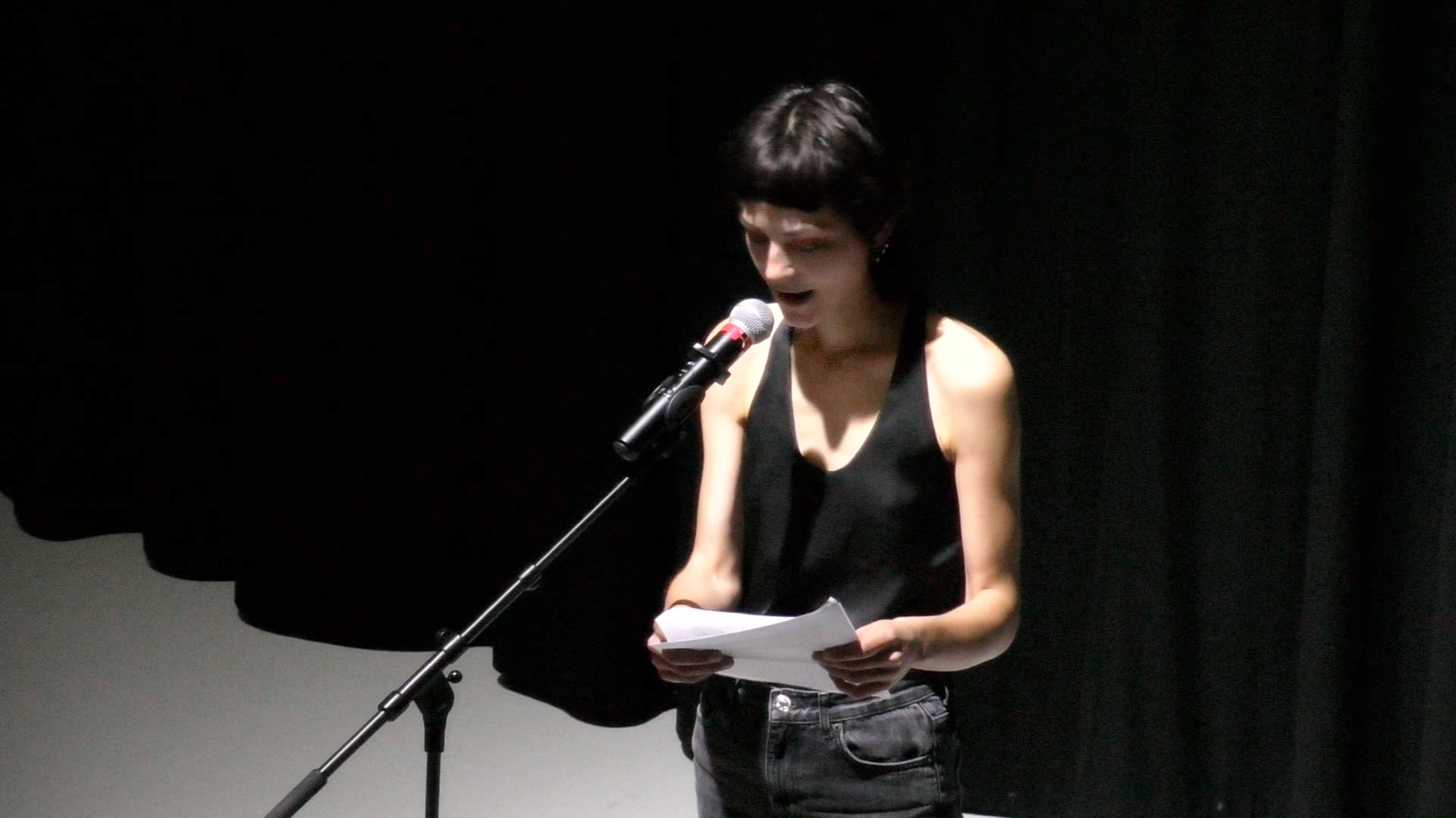 Luzie Meyer speaking into microphone in black box theatre setting