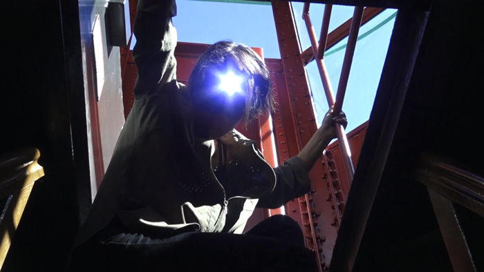 person with had lamo sitting on top of lighthouse with headlamp facing camera