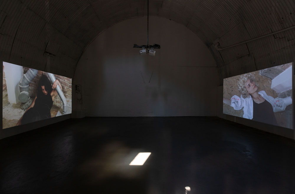 Room with two vdeo projections on two screens opposite of each other.